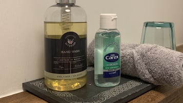 Dos botellas de jabón líquido sobre una superficie de madera, junto con una toalla y un recipiente de vidrio.