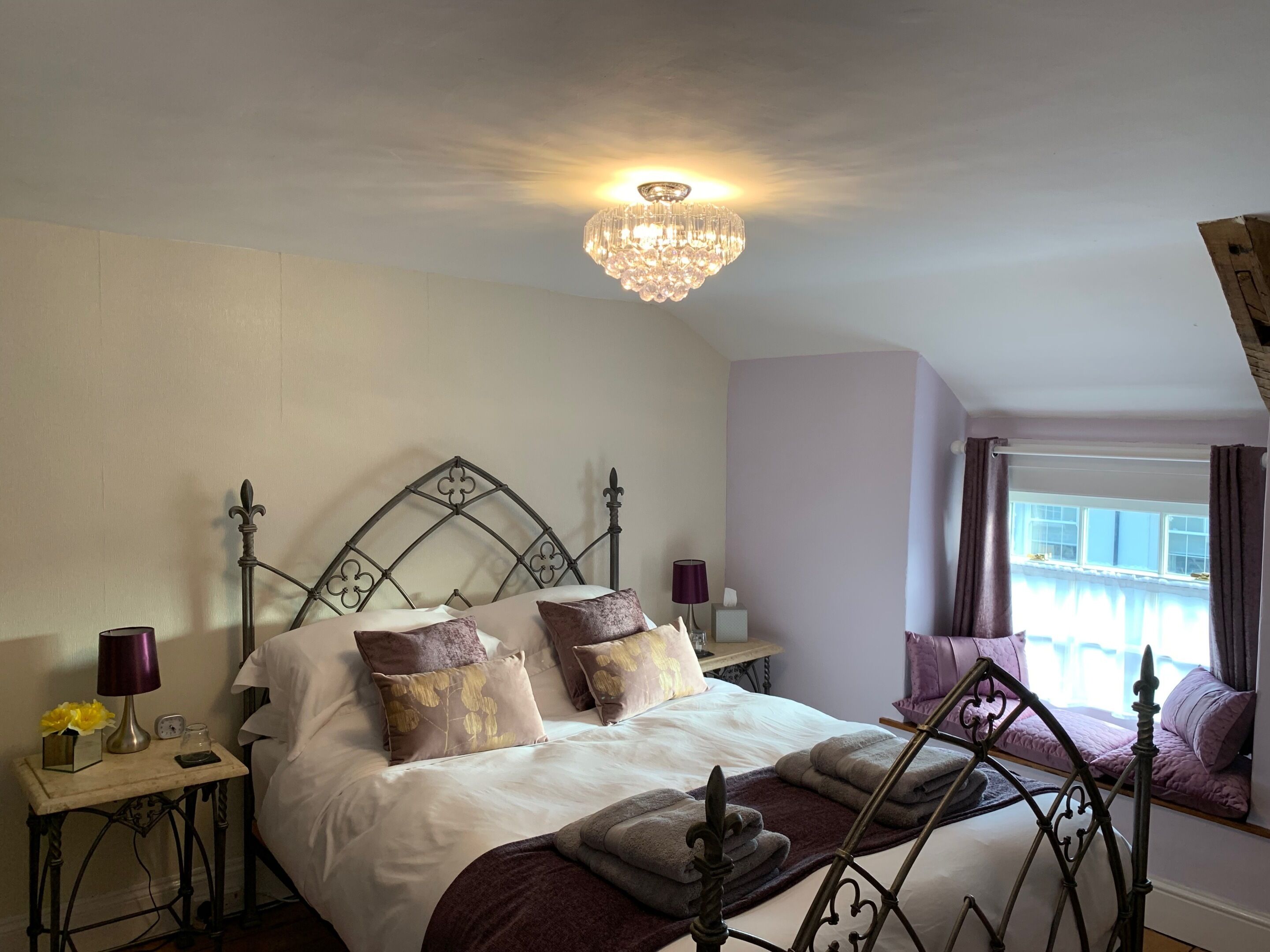 Une chambre à coucher avec un lit, un lustre, une table de chevet et une fenêtre avec des rideaux.