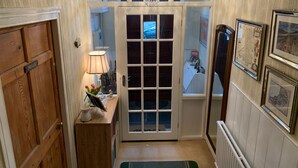 Un pasillo con una puerta de madera que dice “PRIVATE”, una puerta con marco blanco y paneles de vidrio, un candelabro y mapas enmarcados en la pared.