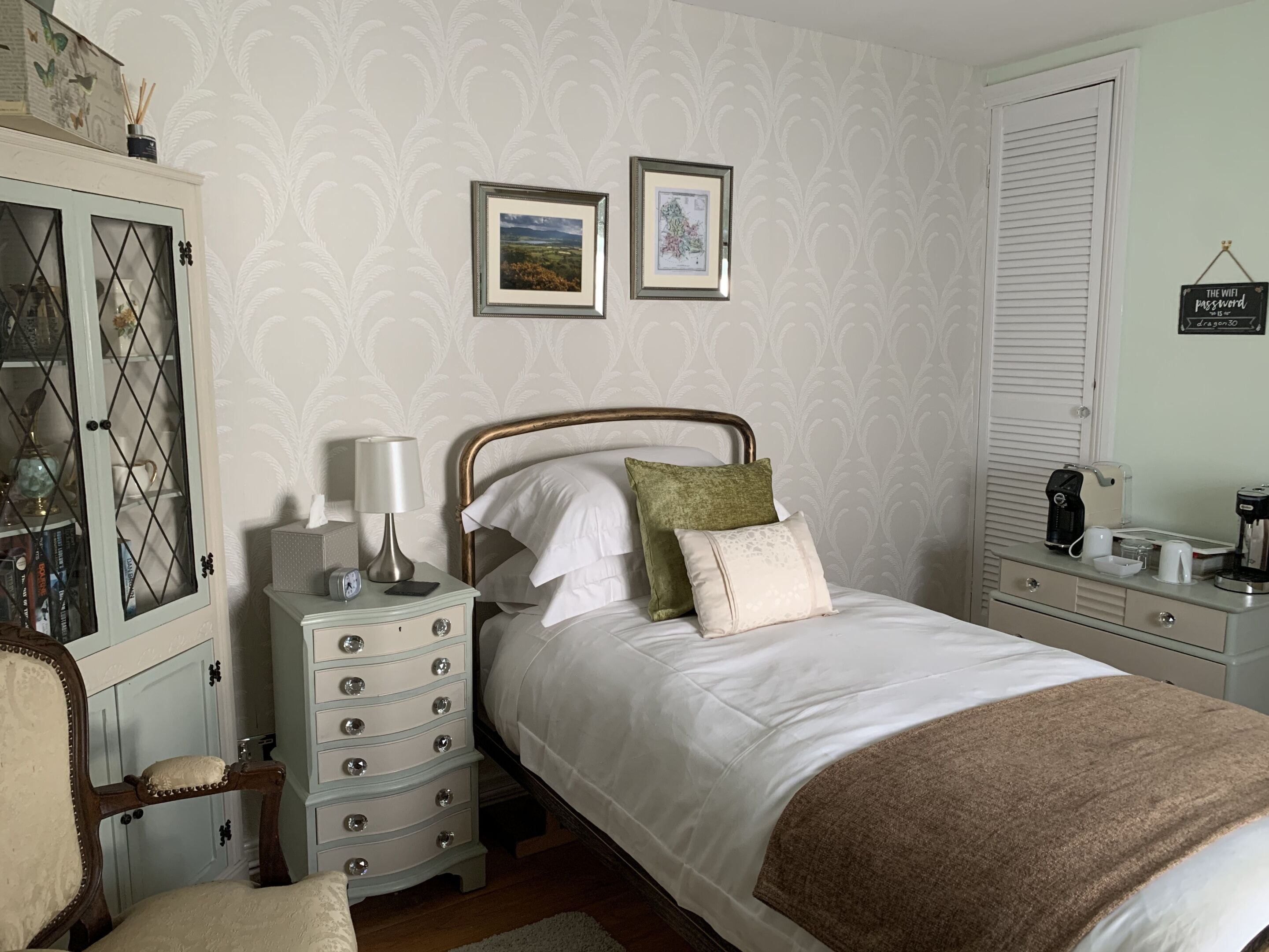 A bedroom with a bed, dresser, nightstand, and a wardrobe. There are two framed pictures on the wall.