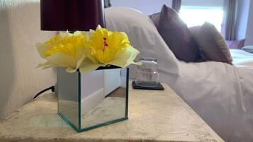 Eine Glasvase mit gelben Blumen auf einem Nachttisch in einem Hotelzimmer.