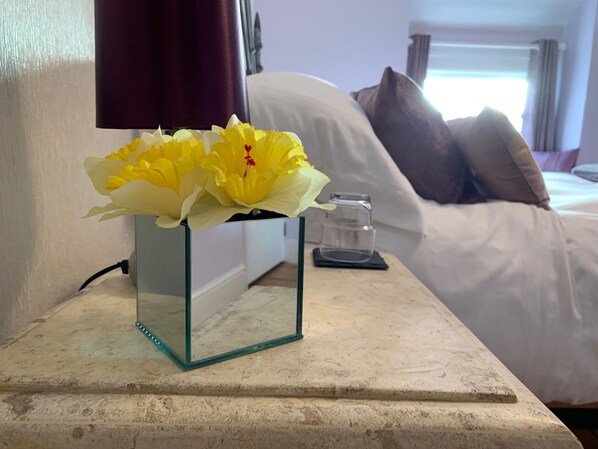 A glass vase with yellow flowers on a bedside table in a hotel room. - Evangelisa (Lampeter)