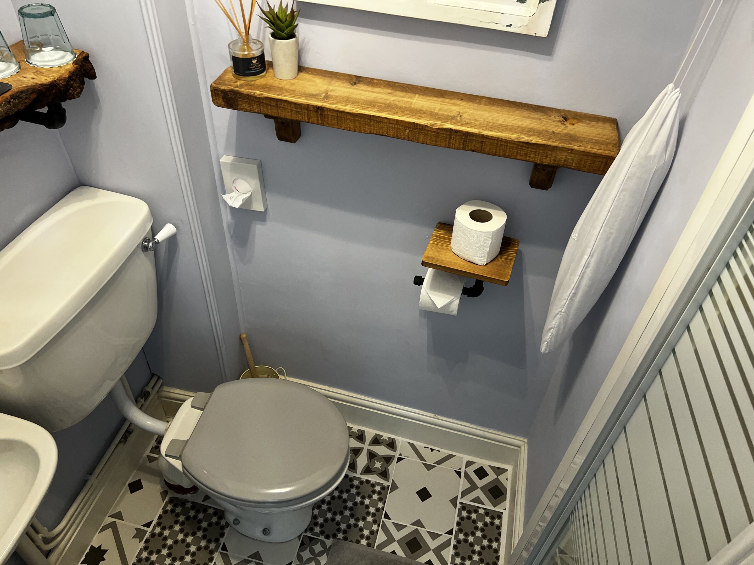 Ein Badezimmer mit Toilette, einem Bidet, einem Regal mit Pflanze und Kerzen sowie einem Toilettenpapierhalter.