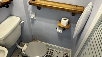 Ein Badezimmer mit Toilette, einem Bidet, einem Regal mit Pflanze und Kerzen sowie einem Toilettenpapierhalter.