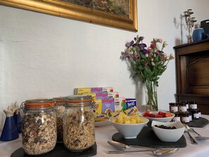Una mesa de desayuno con cajas de cereal, tarros de granola, fruta fresca y frascos de miel.