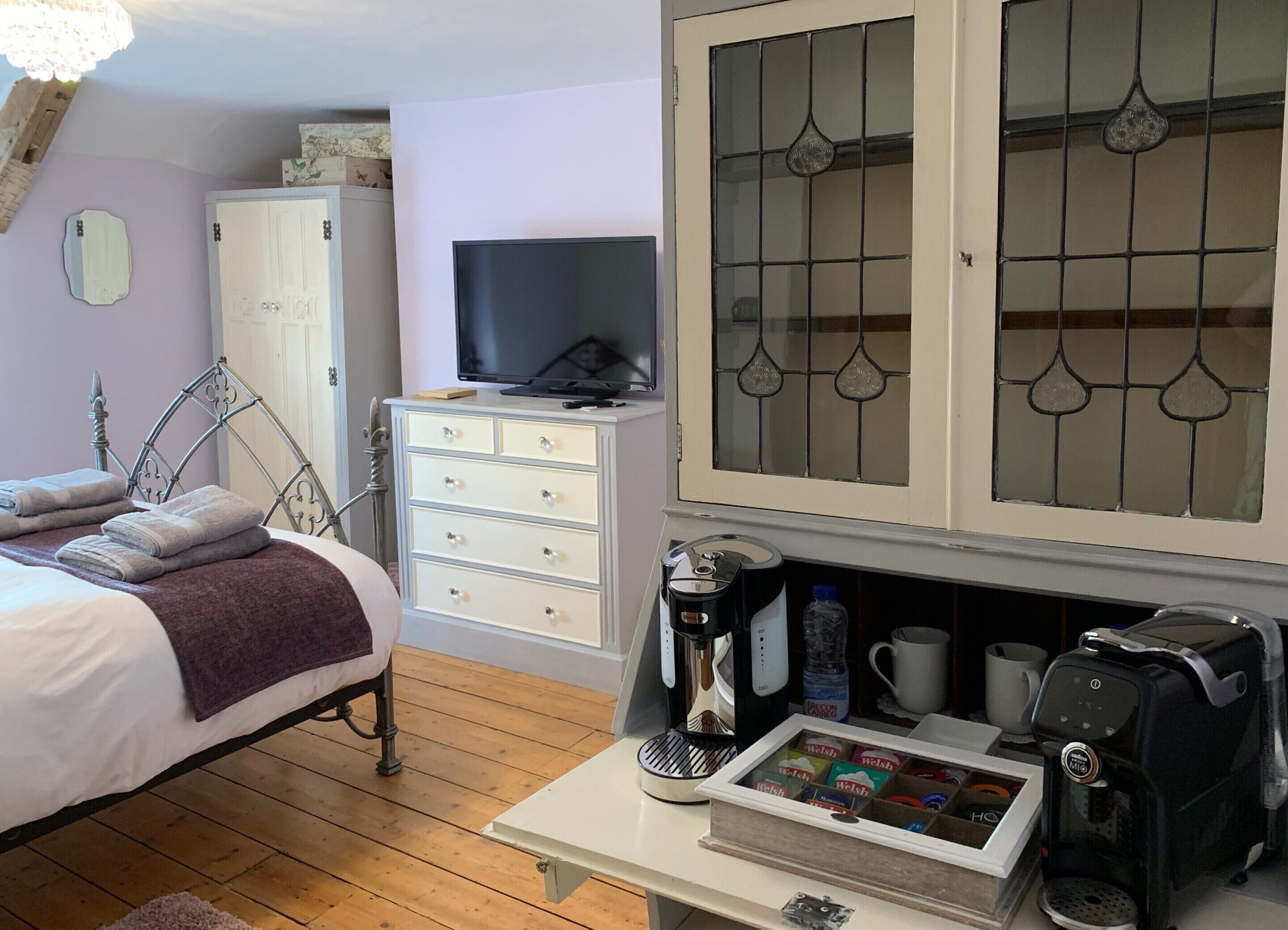 A hotel room with a bed, a dresser, a television, a coffee machine, and a cabinet with glass doors.
