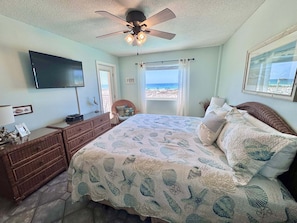 Un dormitorio con cama, cómoda, televisor, ventilador de techo y vista a la playa.