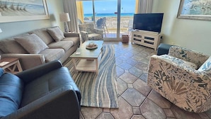 A living room with a sofa, armchair, coffee table, and TV, with a view of the sea through a glass door. - Relax and Catch a couple fish! 🎣 ~ There is something for everyone! (Gulf Shores)
