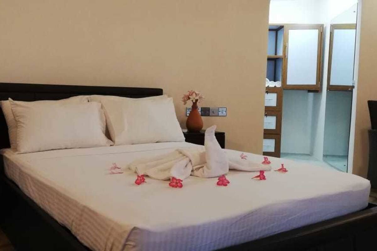 A neatly made bed with white linens and pink flowers, a bedside table with a phone, and a view of a balcony.