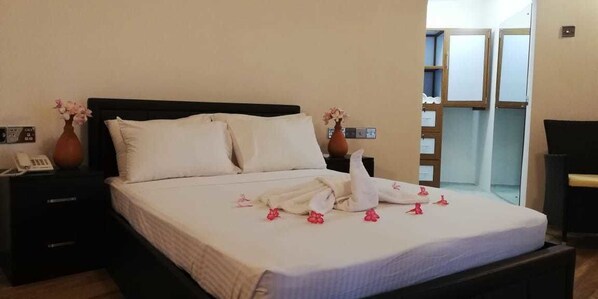A neatly made bed with white linens and pink flowers, a bedside table with a phone, and a view of a balcony. - Seth Dev Lagoon Chalets Kalpitiya (Kudawa)