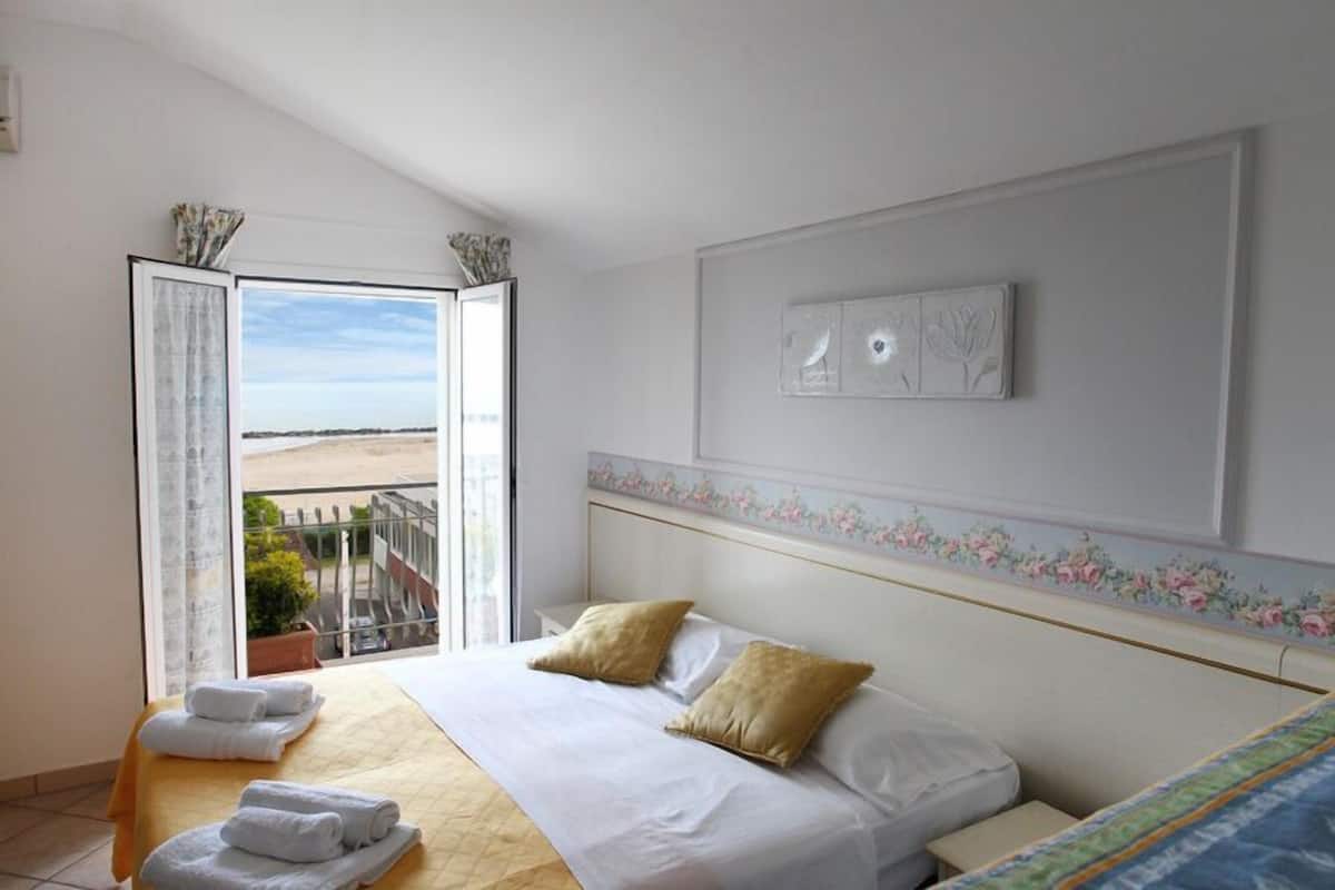 A hotel room with a bed, a view of the sea, and a balcony.