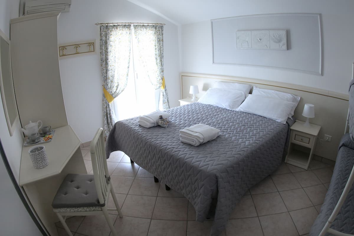A neatly arranged bedroom with a bed, bedside tables, a chair, and a small table with a teapot and cups.