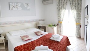 Une chambre d’hôtel avec un grand lit, deux tables de chevet, une commode, un miroir et une fenêtre agrémentée de rideaux à motifs floraux.
