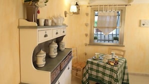 Un coin repas chaleureux avec une nappe à carreaux, une fenêtre ornée d’un rideau en dentelle et une lampe fixée au mur.