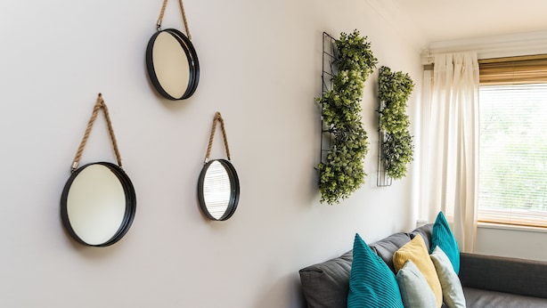Una sala de estar con un sofá gris, cojines verde azulado y amarillos, y tres espejos redondos en la pared.