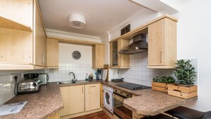 Cocina compacta con armarios de madera, horno empotrado, lavadora y encimera de granito.