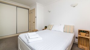 Una cama bien hecha con ropa de cama blanca, una mesita de noche de madera con una planta y un armario con puertas corredizas.