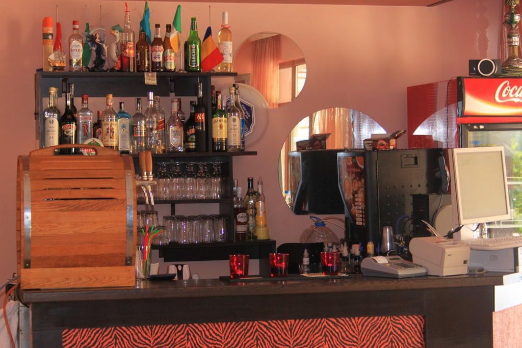 Zona de bar con estantes llenos de botellas de licor, vasos y una máquina expendedora de Coca-Cola.