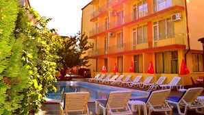 Un hotel con piscina, lettini e bandiere rosse.