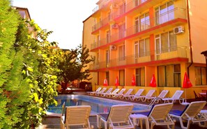 A hotel with a swimming pool, lounge chairs, and red flags. - Ryor (Nessebar)
