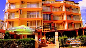 Un hotel a più piani con balconi, un cartello con la scritta 'RYOR' e un ristorante con un ombrello verde.