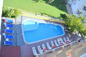 En vy från ovan av ett hotells poolområde med en rektangulär pool, solstolar och en byggnad i bakgrunden.