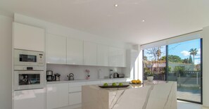 Une cuisine moderne avec des meubles blancs, un Ăźlot en marbre et une grande porte-fenĂȘtre coulissante donnant sur lâextĂ©rieur.