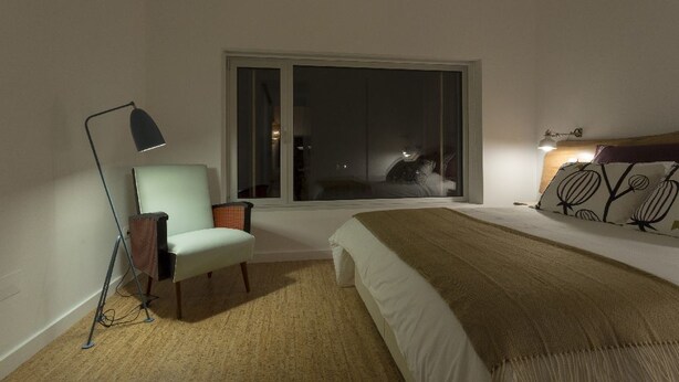 A bedroom with a bed, a chair, a floor lamp, and a window. - Sete Cidades Lake Lodge (Ponta Delgada)