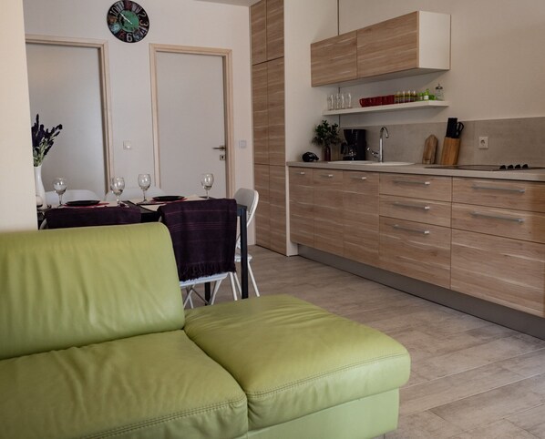 A modern kitchen with wooden cabinets and a built-in stove. There is a dining area with a table and chairs, and a green sofa in the foreground. - New family apartment with terrace 4+2 (Povljana)