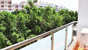 En balkon med gelænder i metal, der udover et række hvide bygninger og frodigt grønt løv.