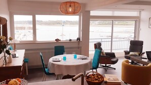Un espace repas comprenant une table ronde, des chaises et une vue sur une étendue d’eau, grâce à de grandes fenêtres.