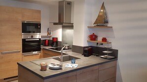 Une cuisine moderne dotée d’appareils électroménagers en acier inoxydable, de meubles en bois, d’un four encastré, d’un four à micro-ondes, d’une machine à café et d’une petite étagère ornée d’objets décoratifs.
