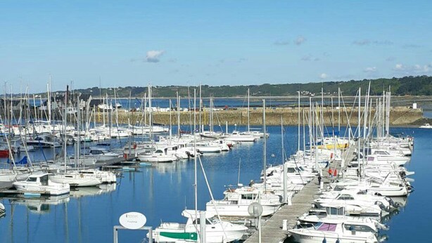 Un port de plaisance où de nombreux bateaux sont amarrés dans des eaux calmes, entouré d’un paysage vallonné.