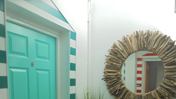 A teal door, a potted plant, a mirror, and a small table with a rug in front. - Pebbles. The Beach House, apartment in central Eastbourne with private parking (Eastbourne)