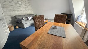 A cozy living room with a wooden dining table, a grey sofa, and a woven chair. - Pebbles. The Beach House, apartment in central Eastbourne with private parking (Eastbourne)