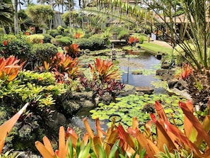 Stroll through a tranquil garden oasis with lush greenery and a serene pond, featuring a picturesque bridge and a traditional building in the background.