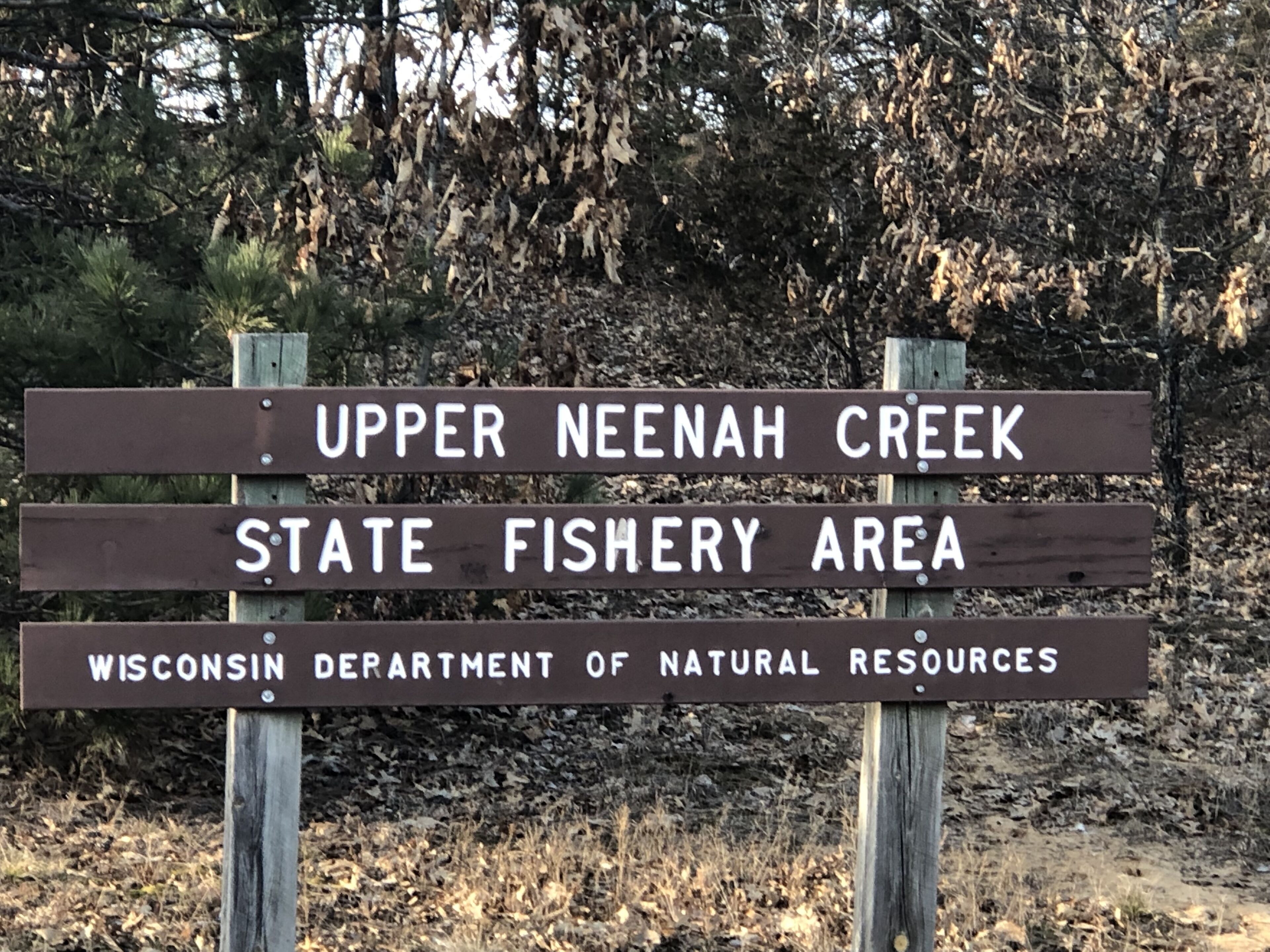 Ein Holzschild mit dem Text, der angibt, dass es sich um das Upper Neenah Creek State Fishery Area handelt, verwaltet vom Wisconsin Department of Natural Resources.