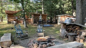 A rustic cabin area with a fire pit, wooden benches, and a pile of firewood. - WI Dells- full Rec lake,swim,boat,ski,UTV,fish,BBQ,sauna,fire pit,hiking,kayak (Oxford)