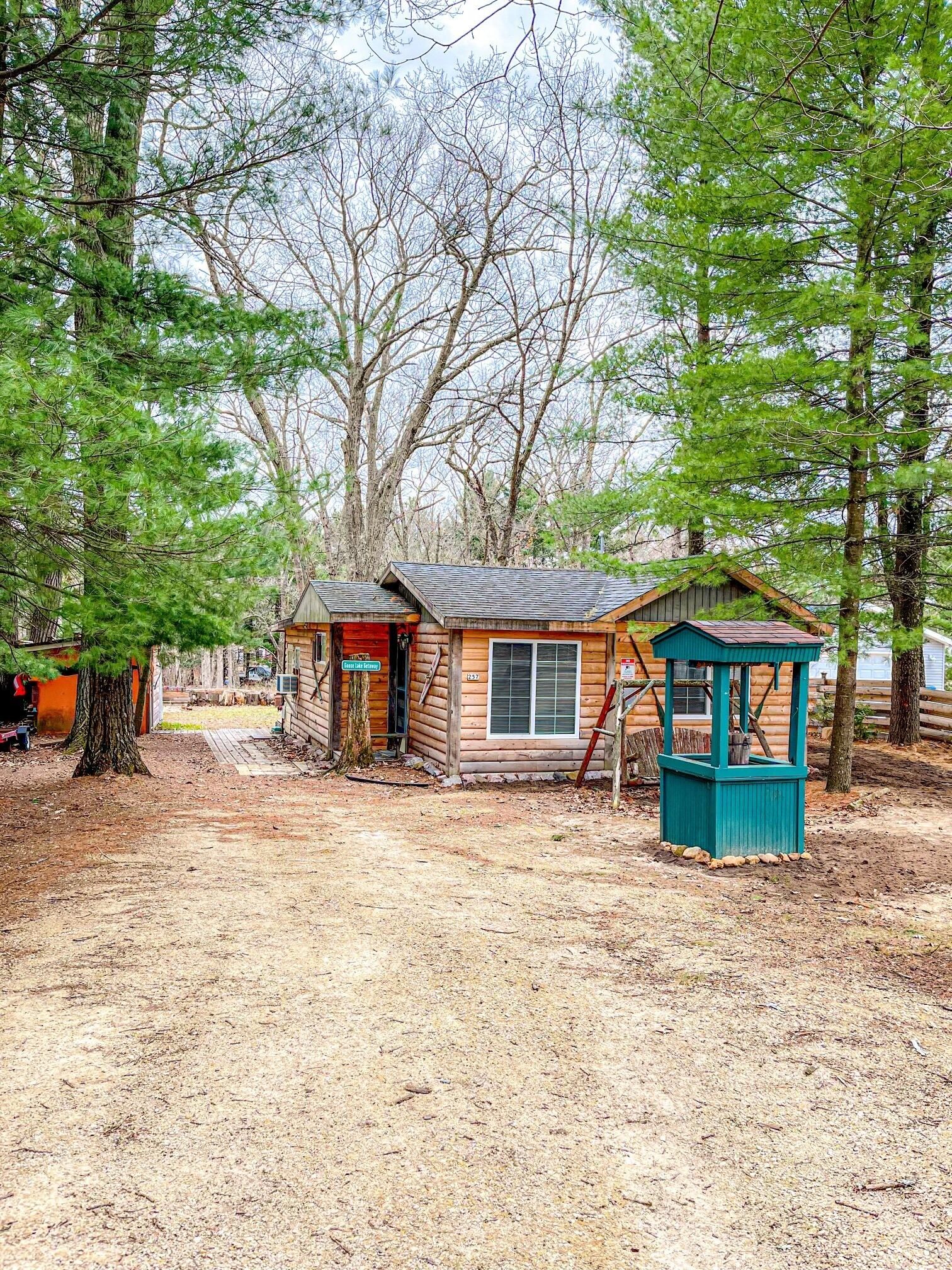 A rustic cabin with a small porch, a wooden structure with a blue roof, and a dirt ground.