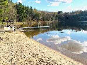 A sandy beach with a wooden bench, a metal dock extending into a calm lake, and a forested shoreline. - Rustic but Modern cabin lake,swim,boat,UTV,fish,BBQ,sauna,fire pit,hiking,kayak (Oxford)