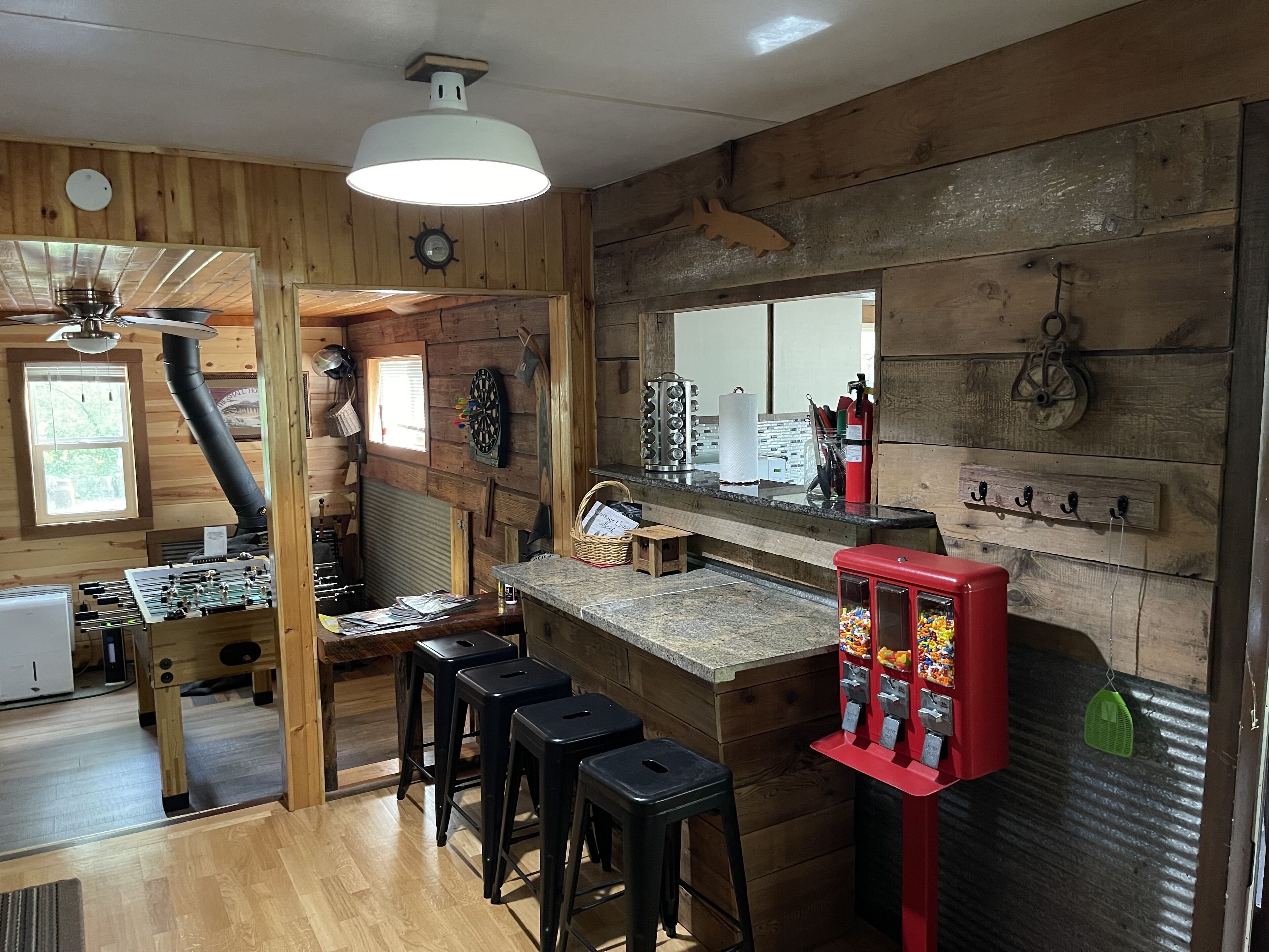 A rustic kitchen with wooden walls, a bar area, stools, and a red vending machine.