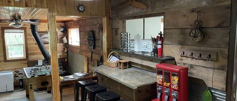 A rustic kitchen with wooden walls, a bar area, stools, and a red vending machine.