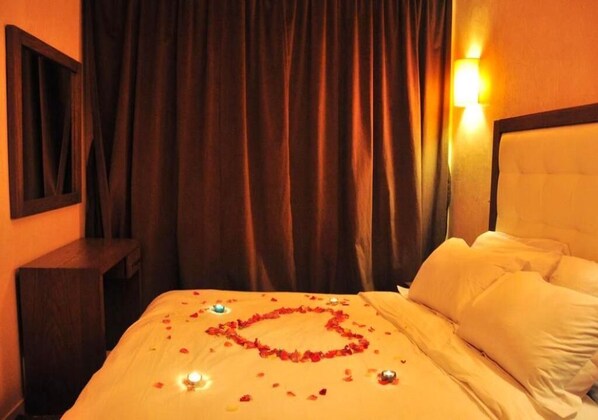 A hotel room with a bed, a nightstand, a wall-mounted lamp, and a curtain.
