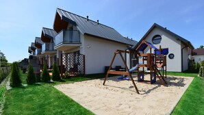 Una casa moderna con un patio trasero grande, un columpio y un tobogán.