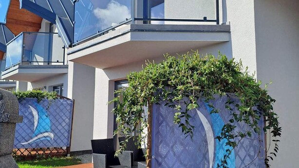 Una casa moderna con terraza de madera, mobiliario exterior y una pared decorativa con diseño de ola.