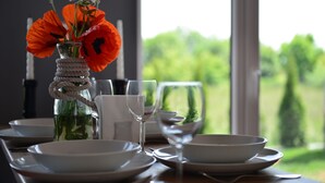 Una mesa vestida con platos, tazones y un vaso de agua blancos. Un jarrón con flores anaranjadas está sobre la mesa.