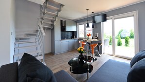 Una cocina moderna con una escalera, un área de comedor con sillas anaranjadas y un gran ventanal con vistas a la vegetación.