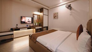A hotel room with a bed, a desk with a flat-screen TV, a mirror, a wall-mounted fan, and a small plant. - Khach San Sao (Hanoi)
