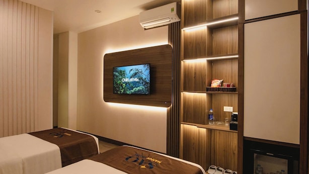 A hotel room with two beds, a TV mounted on the wall, a shelf with snacks, and a shoe rack. - Khach San Sao (Hanoi)