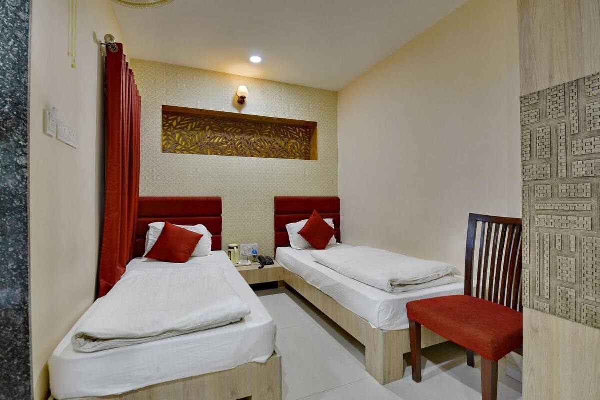 Quarto de hotel com duas camas, uma escrivaninha, uma cadeira e um painel decorativo na parede.